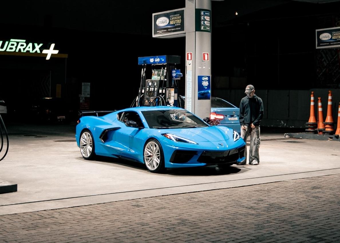 Giovani Brandi ao lado de um Corvette azul em um posto de combustível, à noite